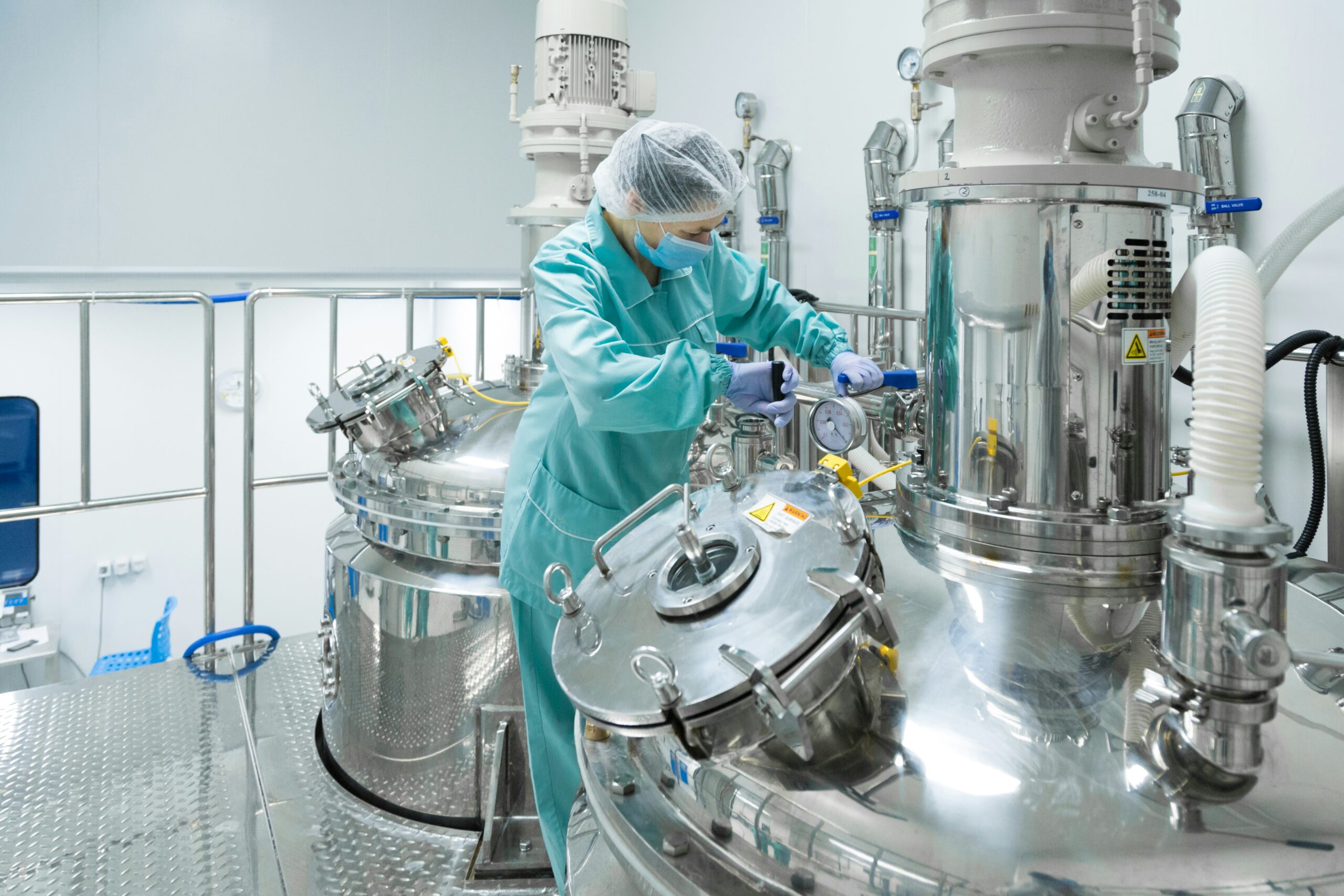 Technician in cleanroom garb operating stainless steel process vessels in a pharmaceutical production suite
